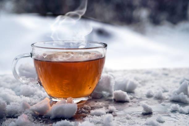 steaming hot tea in a glass cup is standing outside on a cold winter day with snow, copy space, selected focus